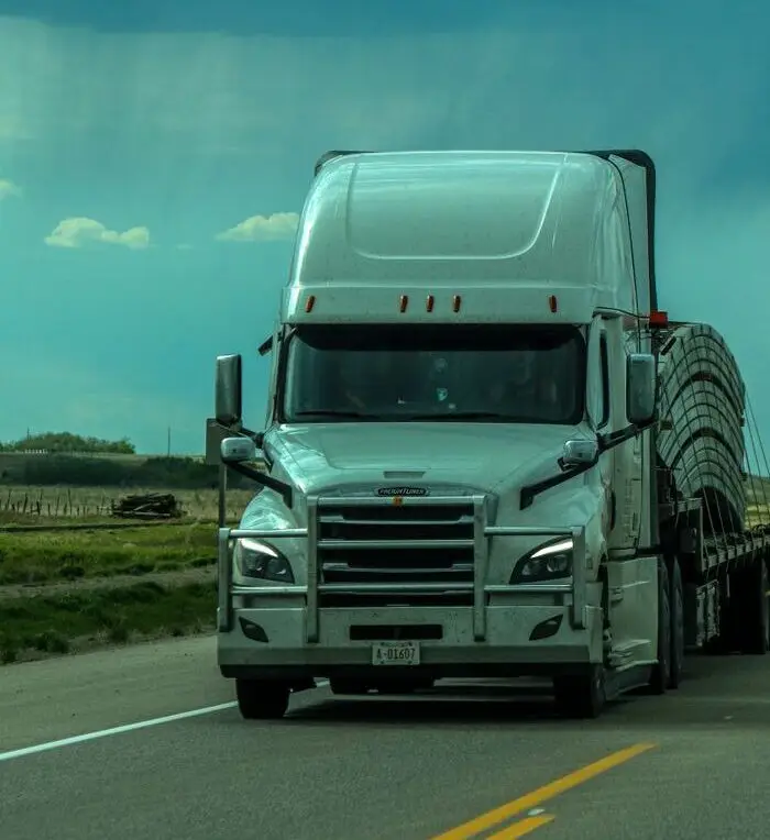 A white semi-truck travels on a highway under a cloudy, dramatic sky.